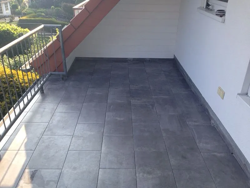 Derselbe Balkon nach der Sanierung mit großen grauen Fliesen.